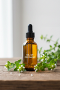 Premium amber glass dropper bottle of Oil of Oregano surrounded by fresh oregano sprigs and white flowers on a rustic wooden surface